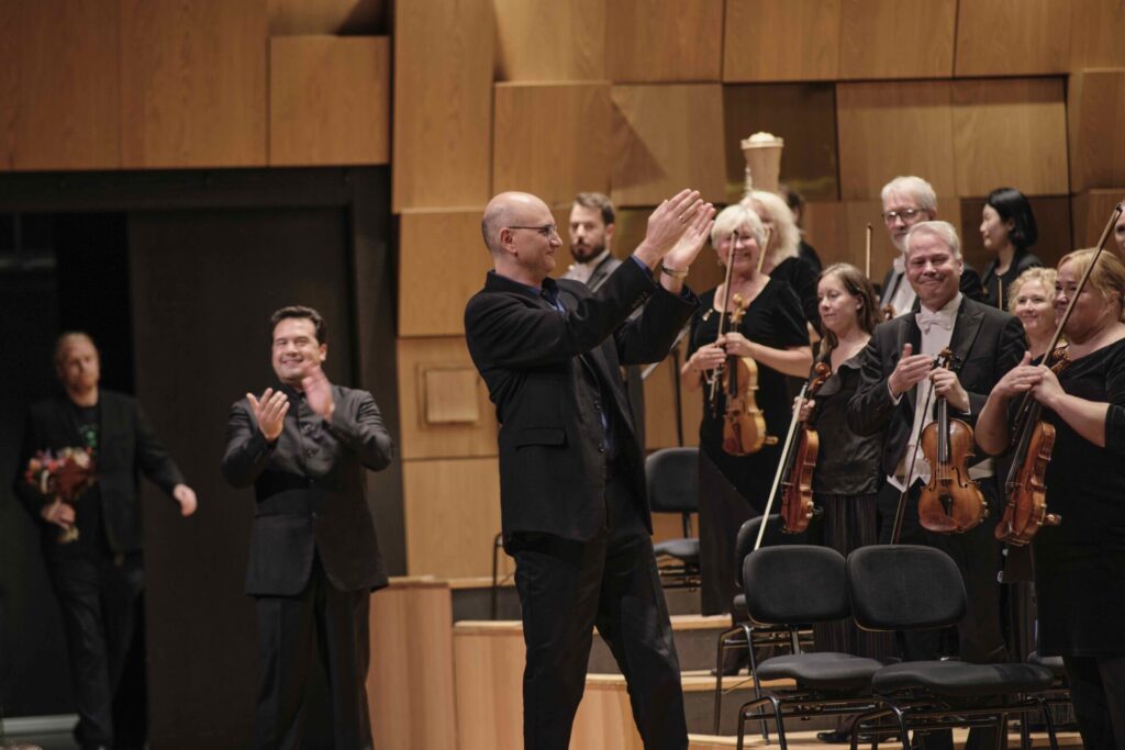 classical contemporary composer Kareem Roustom standing in front of the symphonic orchestra perfomers