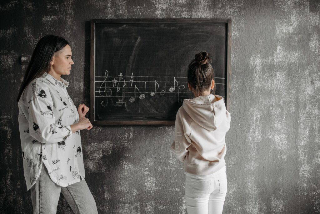 A mother instructs her daughter in music notation at a blackboard, fostering learning.