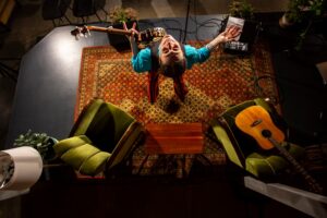 Guitarist on stage looking up at the camera with a colorful carpet uner his feet.
